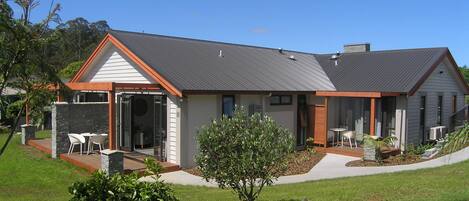 A modern two-story house with a covered patio, a small garden, and a lawn.