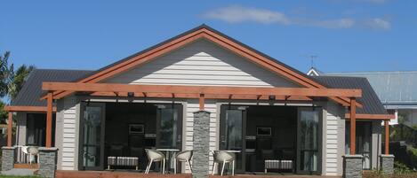 Una casa moderna con porche cubierto, pilares de piedra y un ventanal grande.