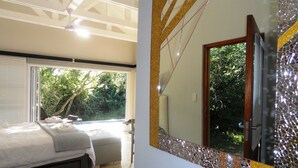 A bedroom with a bed, a window, and a view of trees. - Bushwillow Collection (Hluhluwe)