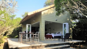 A poolside area with a wooden deck, a table with chairs, and a bedroom visible through an open door. - Bushwillow Collection (Hluhluwe)