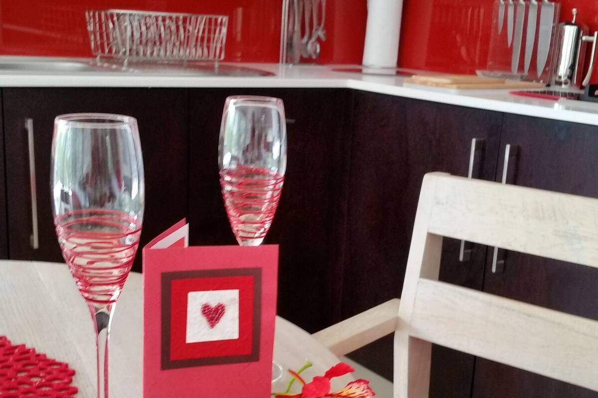 A dining table with two wine glasses, a red card, and a chair with a red cushion.