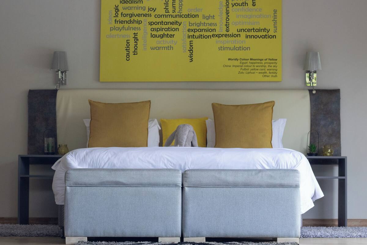 A hotel room with a large bed, two nightstands, and a wall-mounted artwork detailing the symbolism of the color yellow.