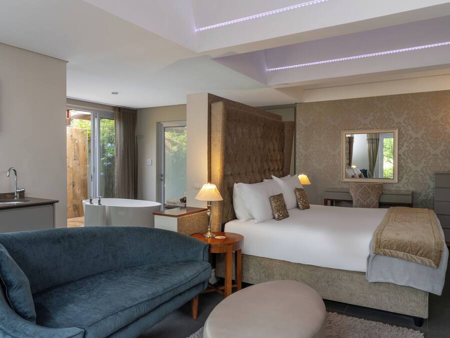 A modern bedroom with a bed, bedside tables, a sofa, and a bathroom.