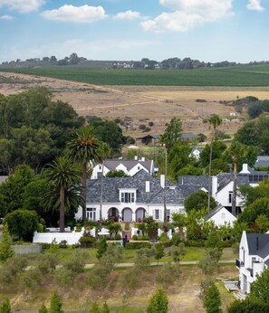 Une grande maison blanche avec un toit gris, entourée de verdure et située dans un paysage vallonné.