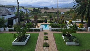 A landscaped garden with a swimming pool, palm trees, and a view of distant hills. - The Wild Mushroom Luxury Country House (Stellenbosch)