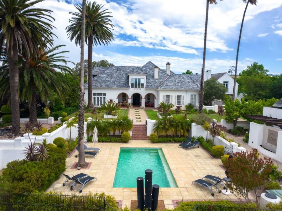 Una casa grande con piscina, palmeras y un jardín bien cuidado.
