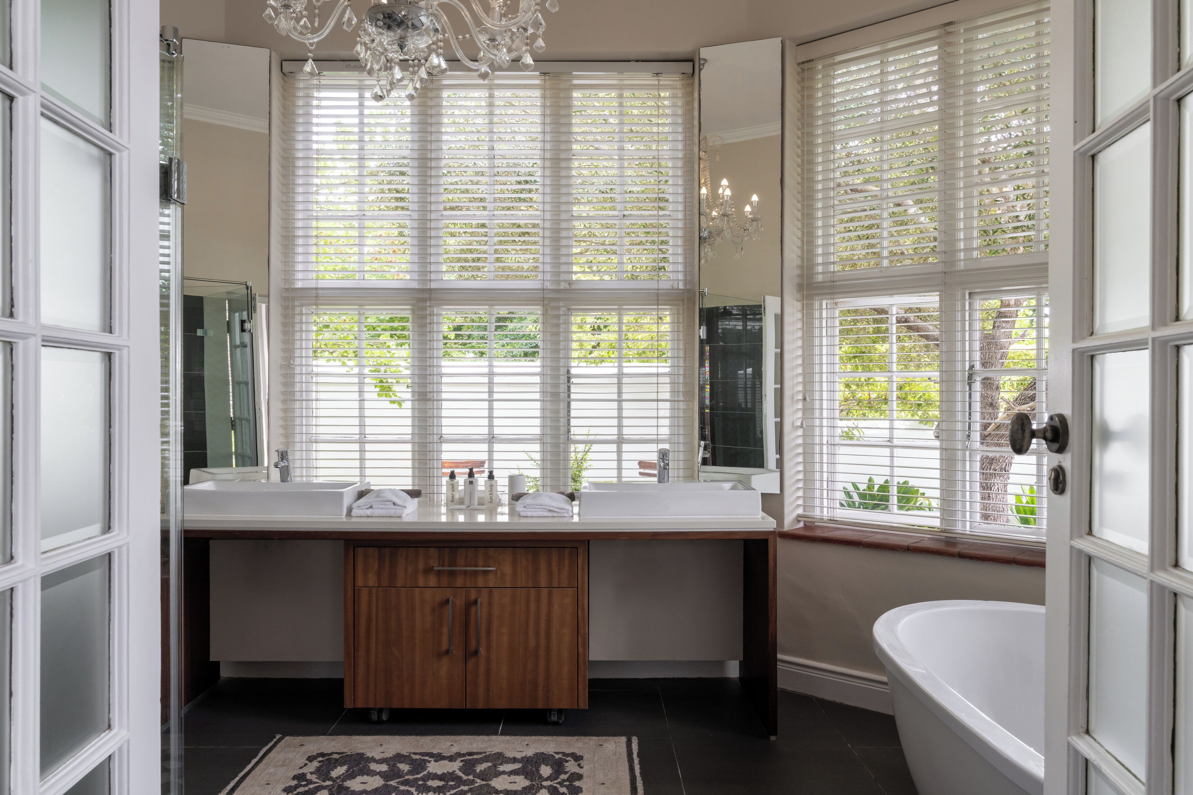 A bathroom with a double sink, a wooden cabinet, a large mirror, a chandelier, and a bathtub.