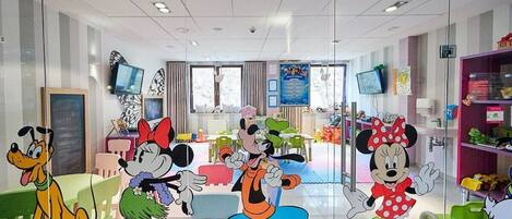 Un salón de juegos para niños con recortes de personajes de caricaturas, mesas, sillas y carteles educativos.