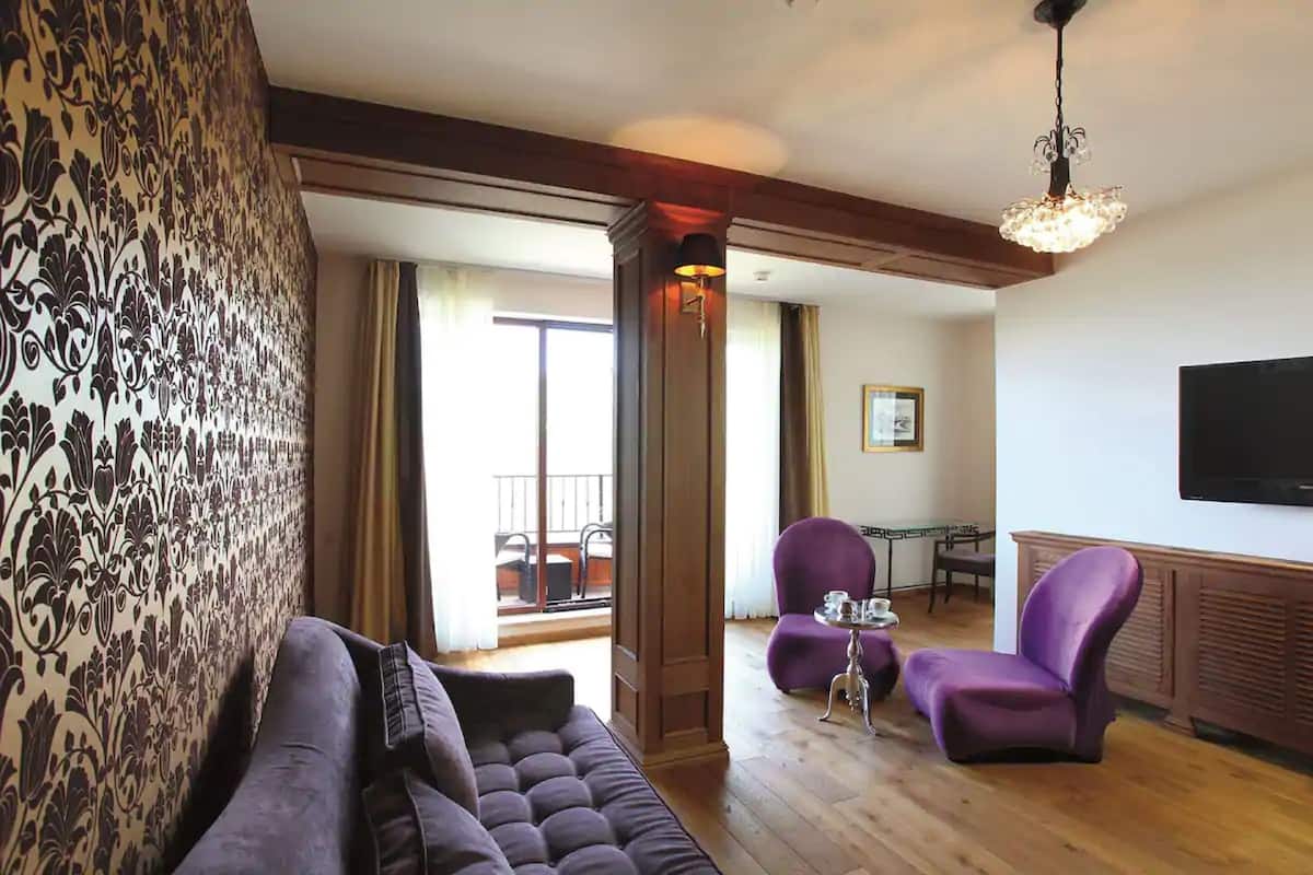 A living room with a patterned wallpaper, a purple sofa, a chandelier, and a television.