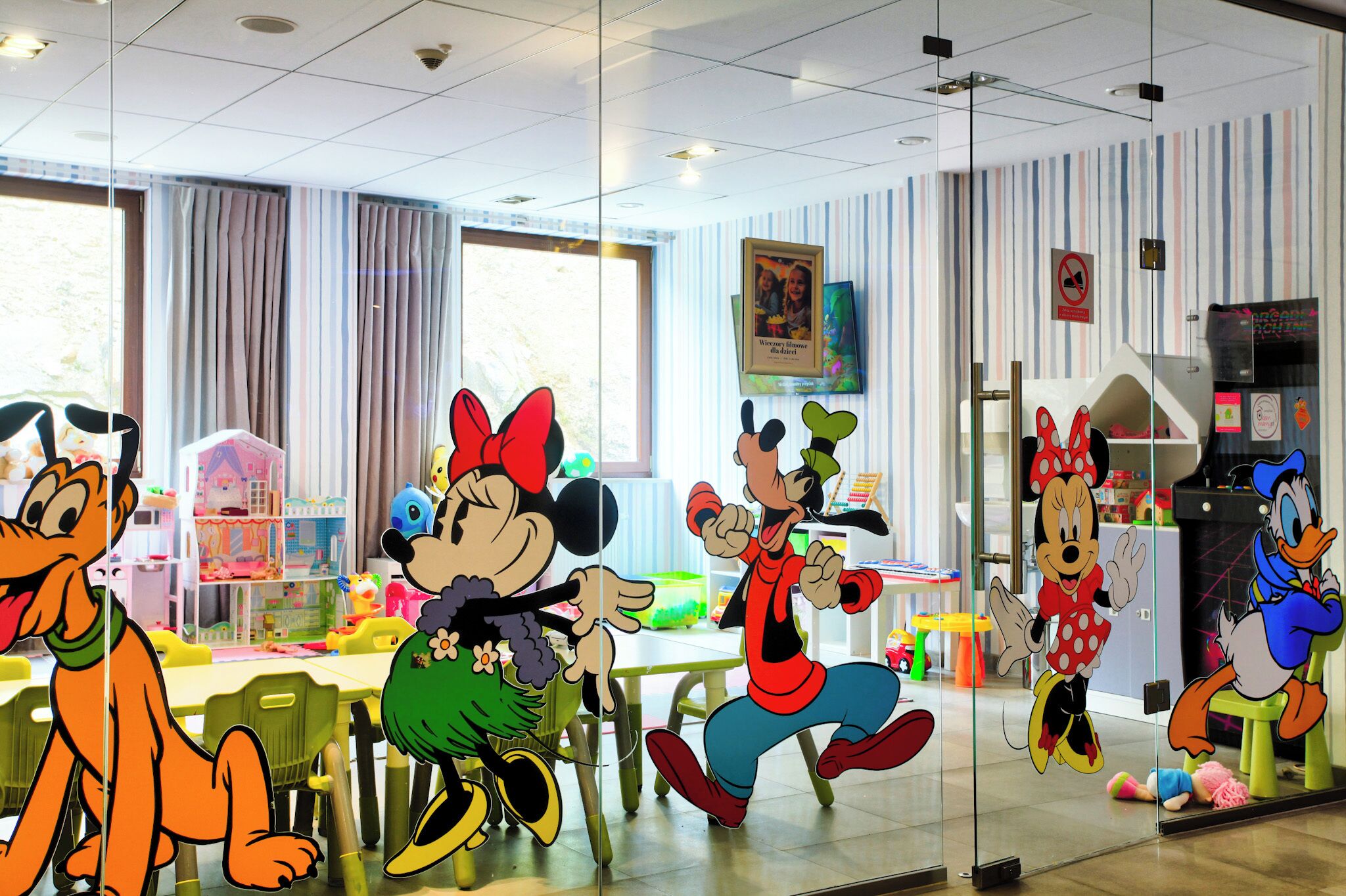 A children's playroom with cartoon character cutouts, a large window, and a striped wall.