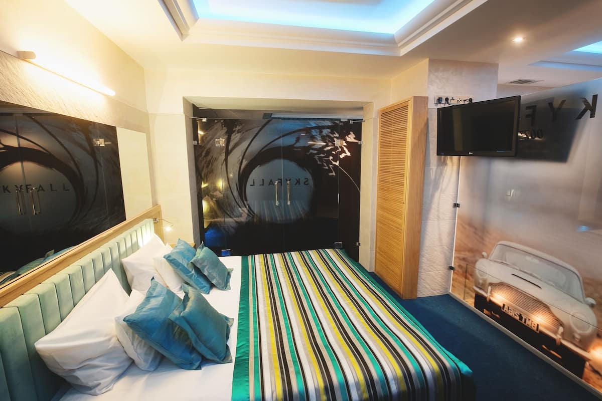 A modern hotel room with a bed, pillows, a television, and a large mirror.