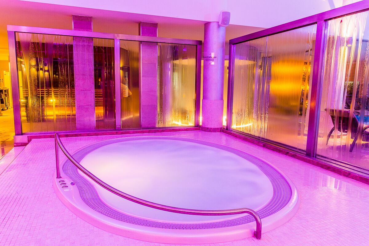 A hot tub with a glass enclosure, surrounded by a tiled floor and a purple-lit interior.