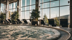 Ett område med ett bubbelbad, solstolar och krukväxter, stora fönster och utsikt över omgivningen.