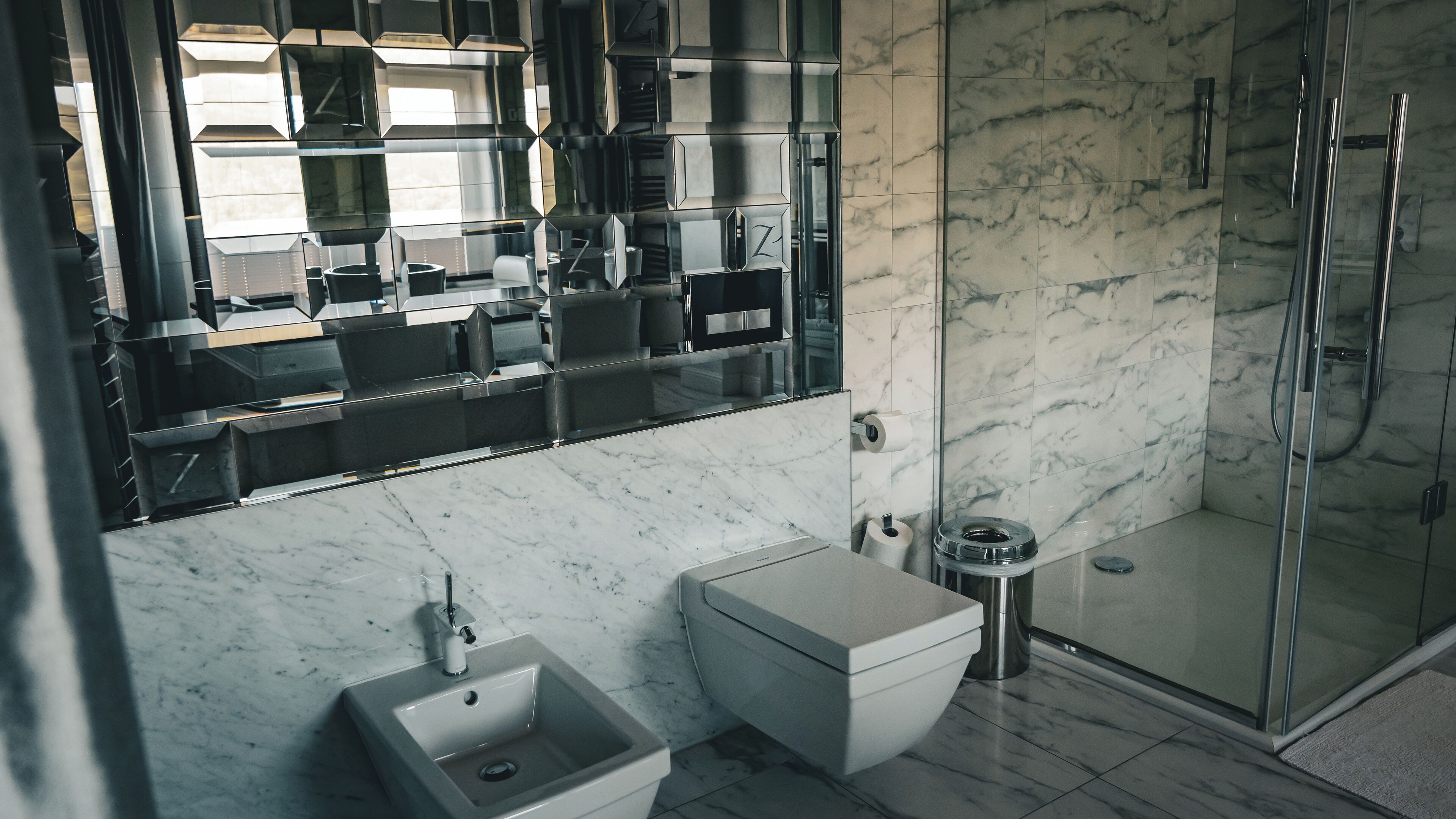 A modern bathroom with a glass shower enclosure, a white toilet, and a sink with a marble countertop.