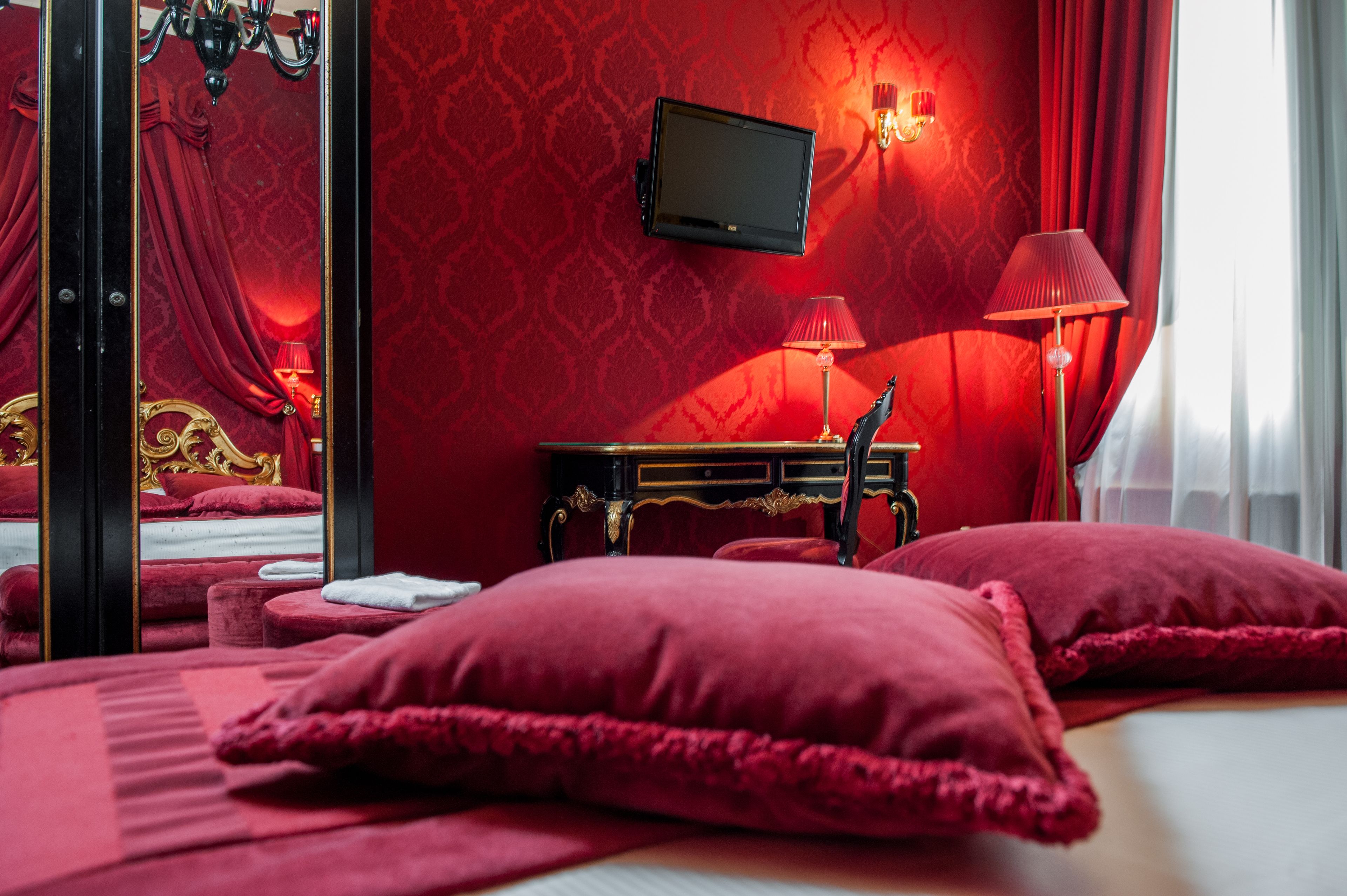 A room with a bed, a television mounted on the wall, a lamp, and a mirror.