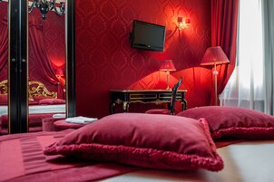 A room with a bed, a television mounted on the wall, a lamp, and a mirror.
