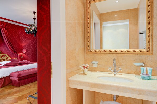 A hotel room with a large bed, a chandelier, a bathroom with a mirror, sink, and toiletries.