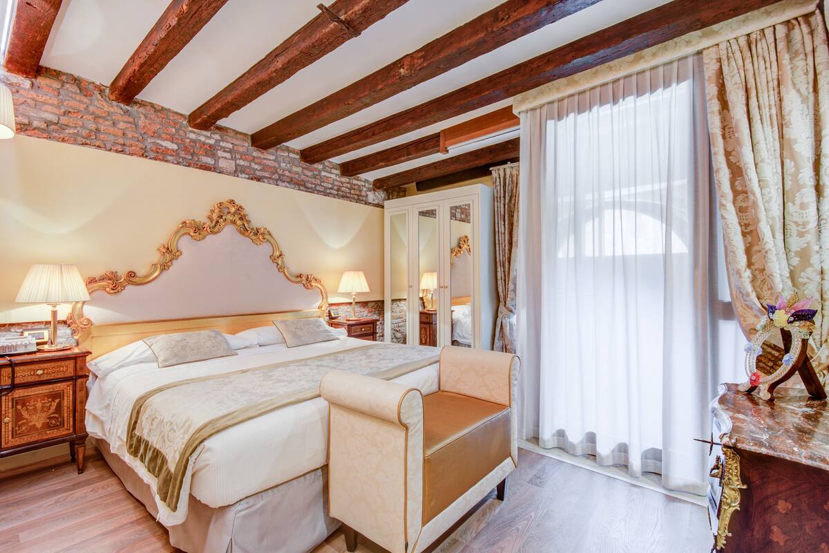 Ein Schlafzimmer mit einem großen Bett, einem Nachttisch, einer Kommode und einem Fenster mit Vorhängen.