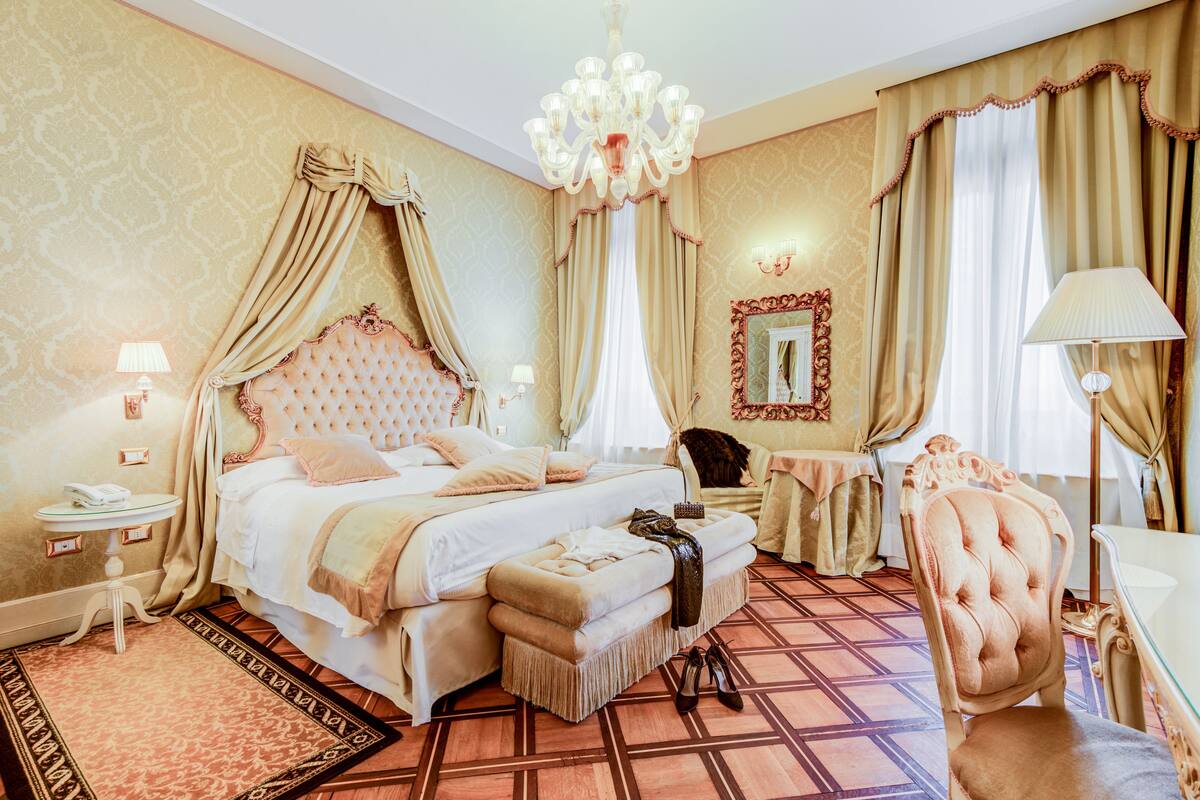 Ein luxuriöses Schlafzimmer mit einem großen Bett, einer Liege, einem Schminktisch mit Spiegel und einer Kristallleuchter.