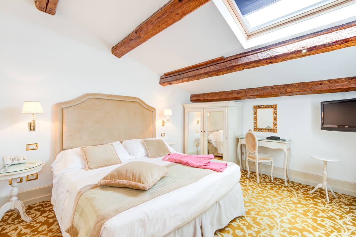 Ein Hotelzimmer mit Bett, Nachttisch, Lampe, Schreibtisch, Stuhl und Fernseher.