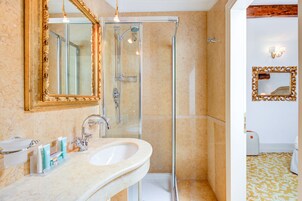 Un baño con cabina de ducha de vidrio, un lavabo con artículos de aseo y un espejo grande y decorativo.