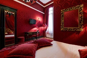 A red-themed hotel room with a large bed, a desk, a chair, and a television.