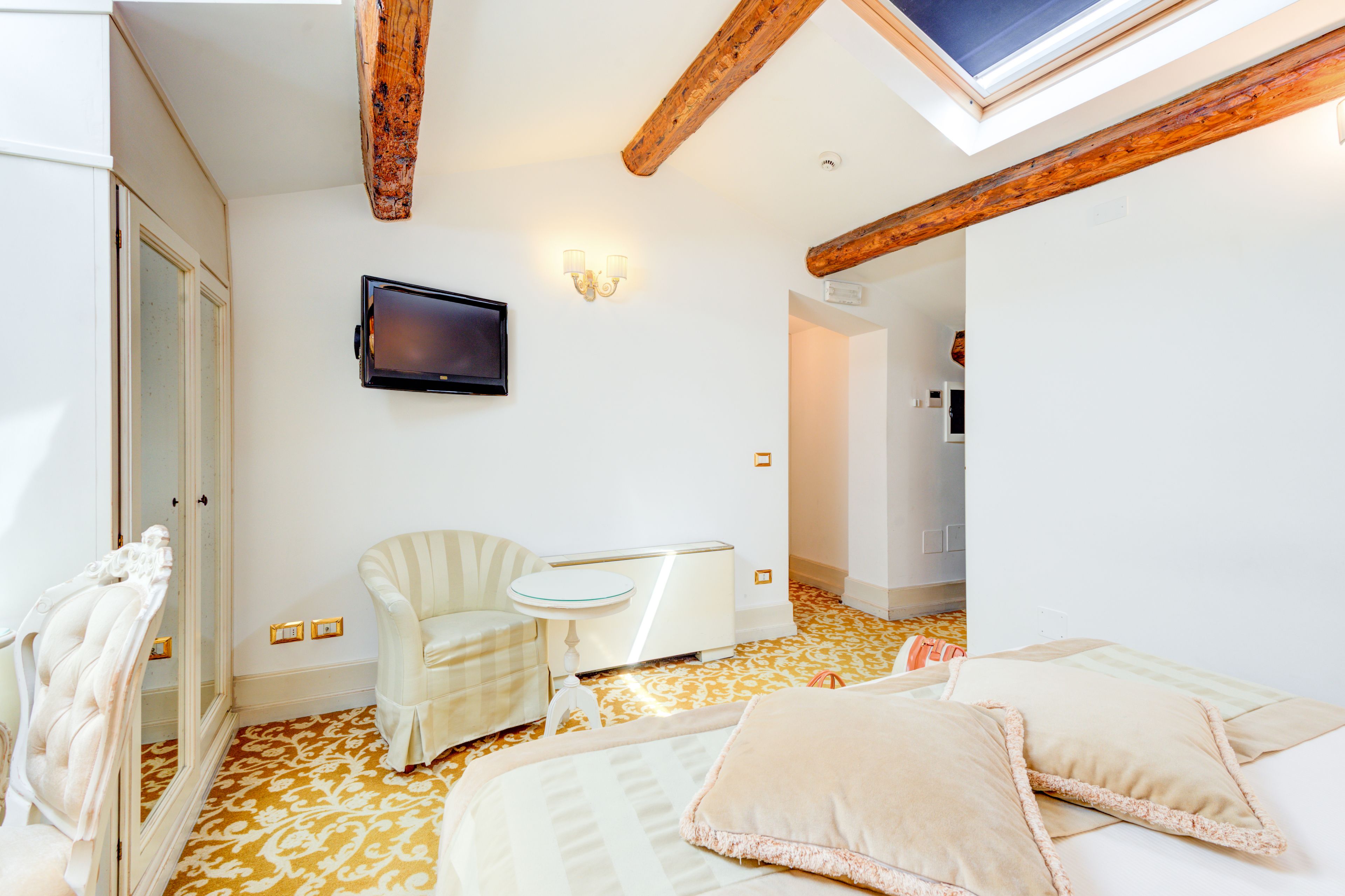 A hotel room with a bed, a chair, a small table, a TV, and a mirror.
