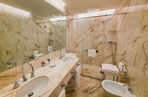 Casa de banho em mármore com duas lavatórios, chuveiro e sanita.
