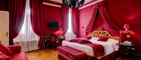 A red-themed bedroom with a bed, a desk, and a television.