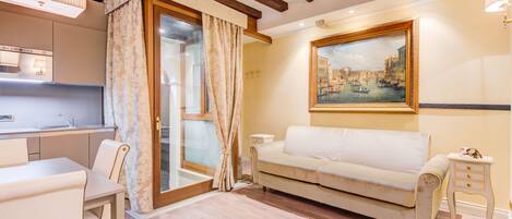 A living room with a sofa, a small table, a glass door, and a painting on the wall.