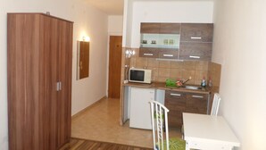 Una cocina compacta con microondas, pileta y heladera pequeña. Se observa un armario de madera y una mesa de comedor con sillas.