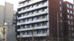 Un edificio de varios pisos con balcones, fachada plana y un área de estacionamiento al frente.