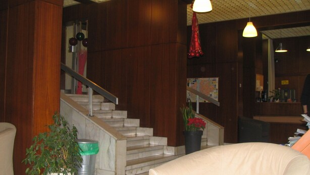 Un vestíbulo con una escalera, una recepción y un sillón color beige.
