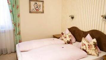 A bedroom with a bed, floral curtains, a framed picture on the wall, and a striped wall pattern.