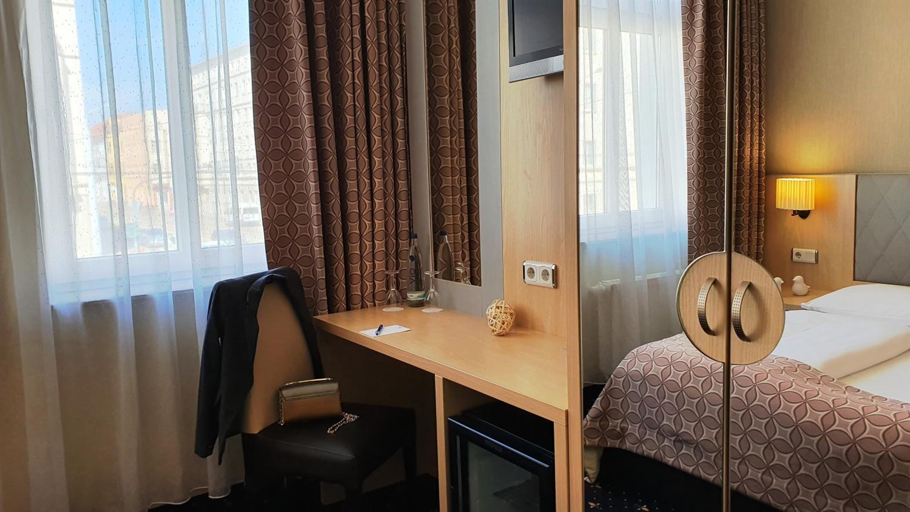 Habitación de hotel con cama, escritorio, silla, televisión y ventana con cortinas.