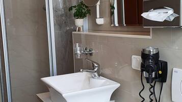Een moderne badkamer met een wit wastafel, een handdouche, een haardroger en een handdoekhouder.