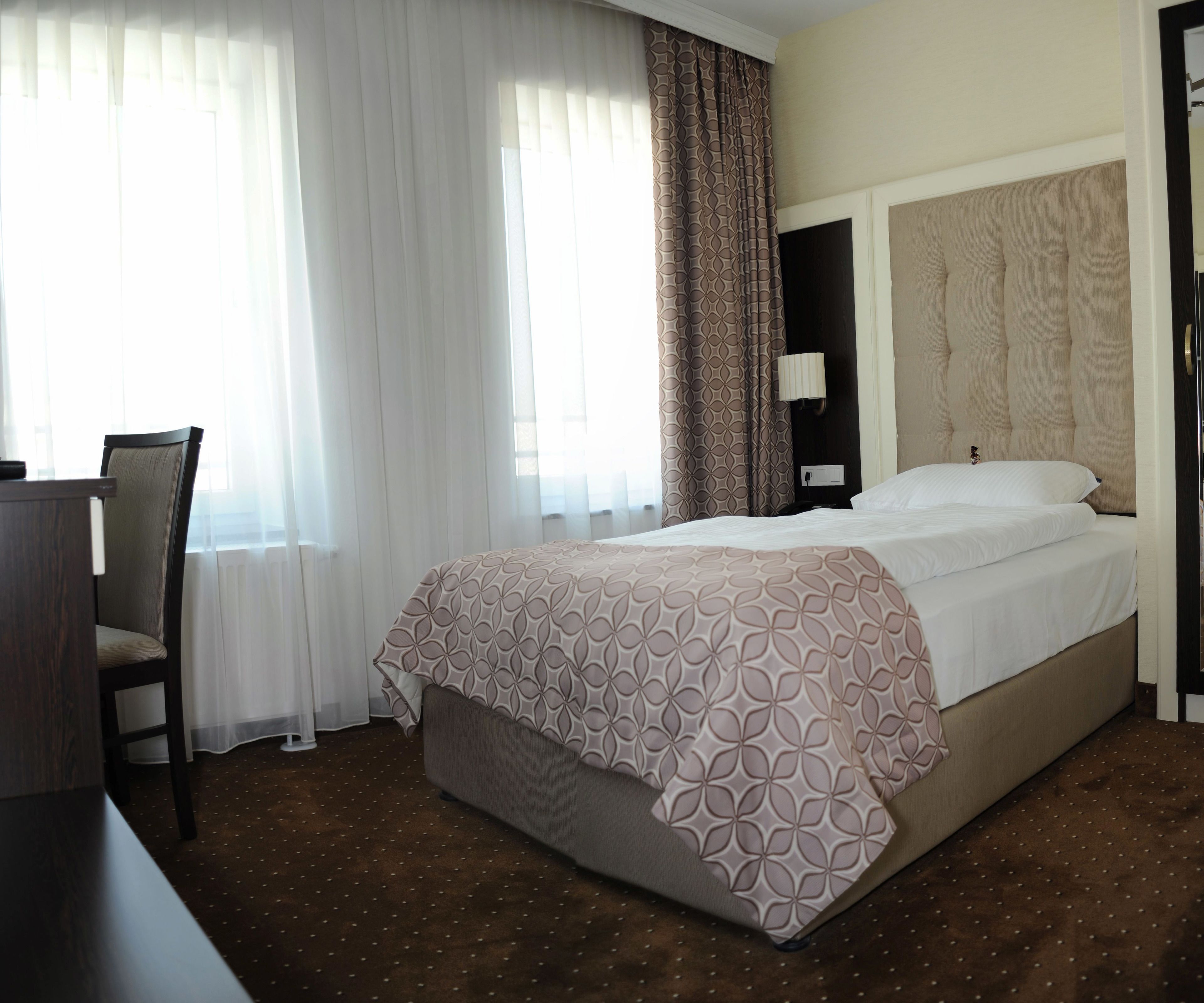 Ein Hotelzimmer mit Bett, Sessel, Schreibtisch und einem Fenster mit Vorhängen.