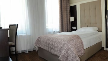Ein Hotelzimmer mit Bett, Sessel, Schreibtisch und einem Fenster mit Vorhängen.