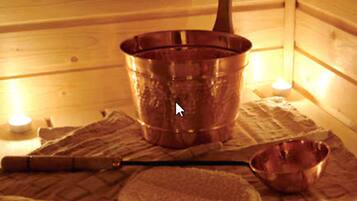 A wooden sauna with a copper pot, a wooden spoon, a towel, and a small bowl on a mat.