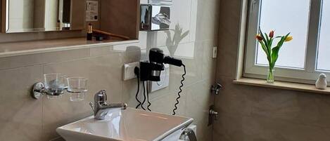 Une salle de bain moderne avec un grand miroir, un lavabo blanc, des toilettes et une fenêtre donnant sur le ciel.
