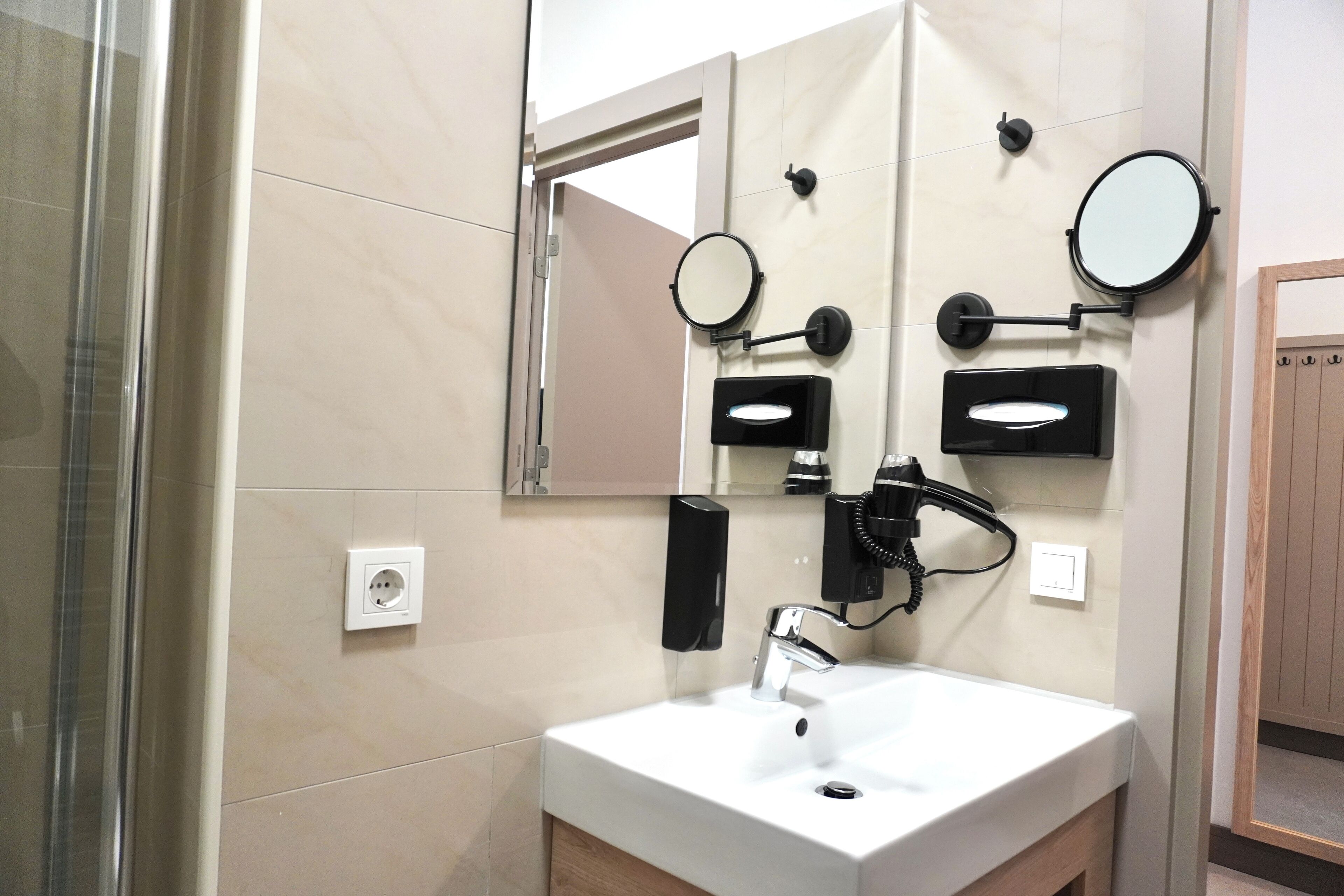 A modern bathroom with a white sink, a mirror, a hairdryer, and a towel dispenser.