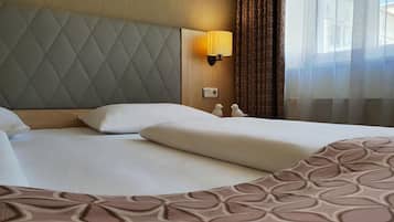 A hotel room with a large bed, a headboard with a diamond pattern, a wall-mounted lamp, and a view through sheer curtains.