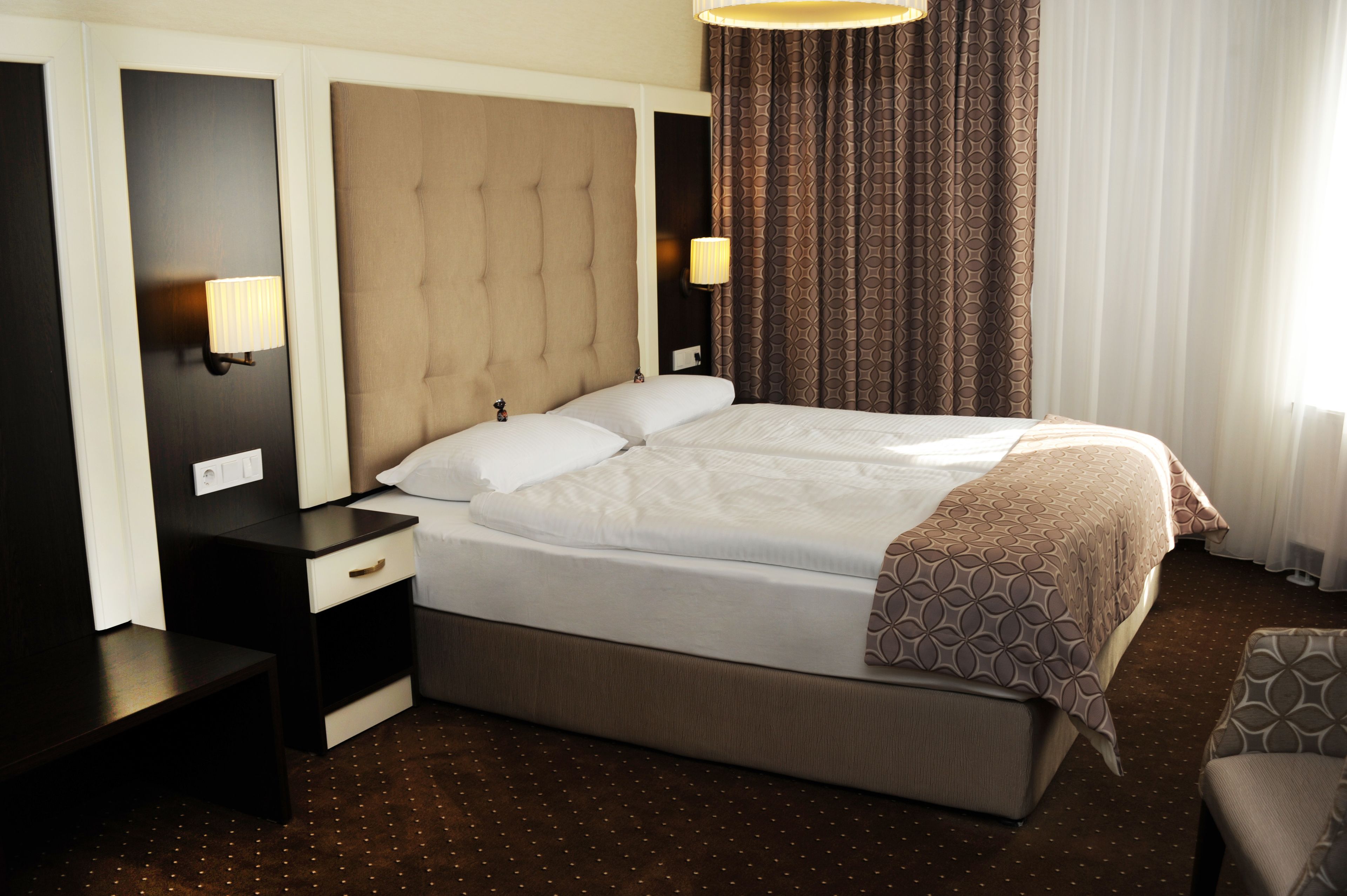 A neatly arranged hotel room with a large bed, bedside tables, a chair, and a patterned throw blanket.