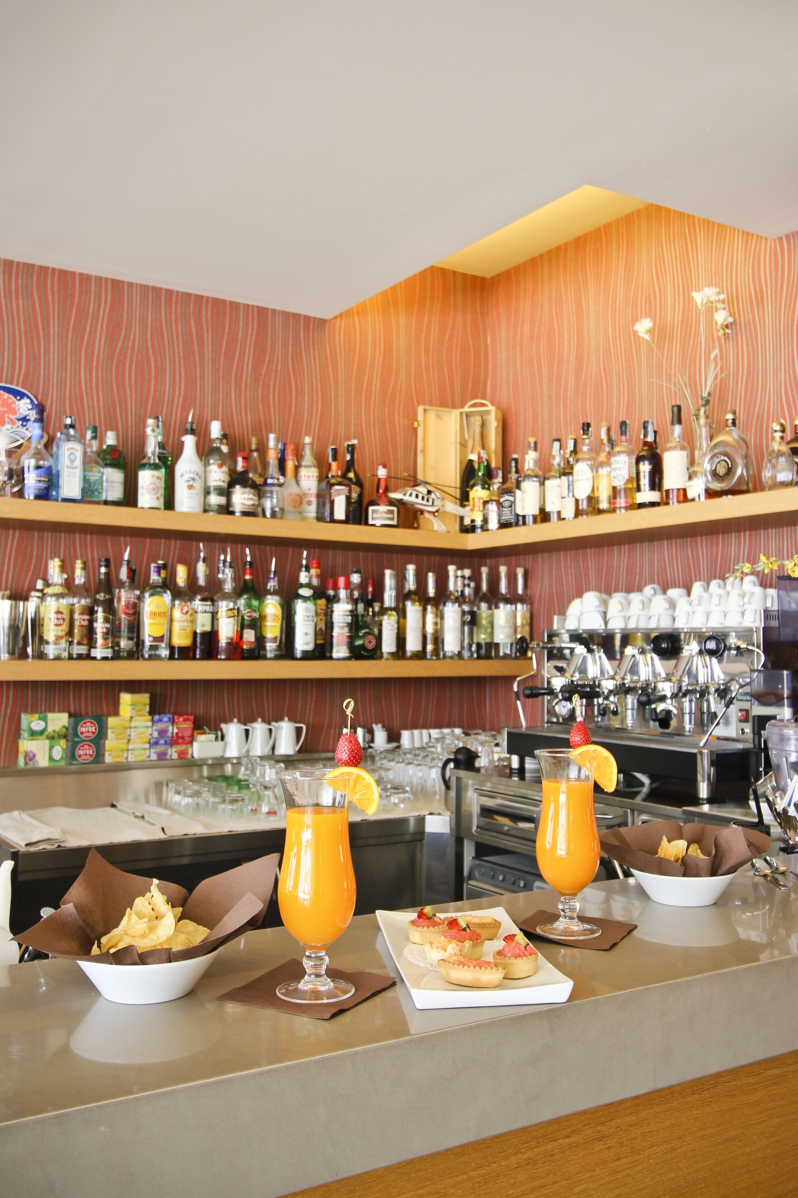 Zona de bar con estantes llenos de botellas de licores, una máquina de café y una barra con aperitivos y bebidas.