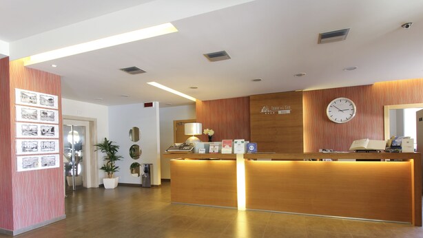 A hotel reception area with a wooden reception desk, a clock, and a wall-mounted sign. - Torre del Sud Hotel (Modica)