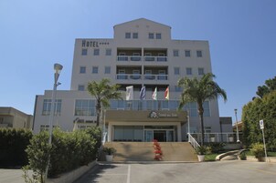 A multi-story hotel with balconies, a staircase leading to the entrance, and flags.