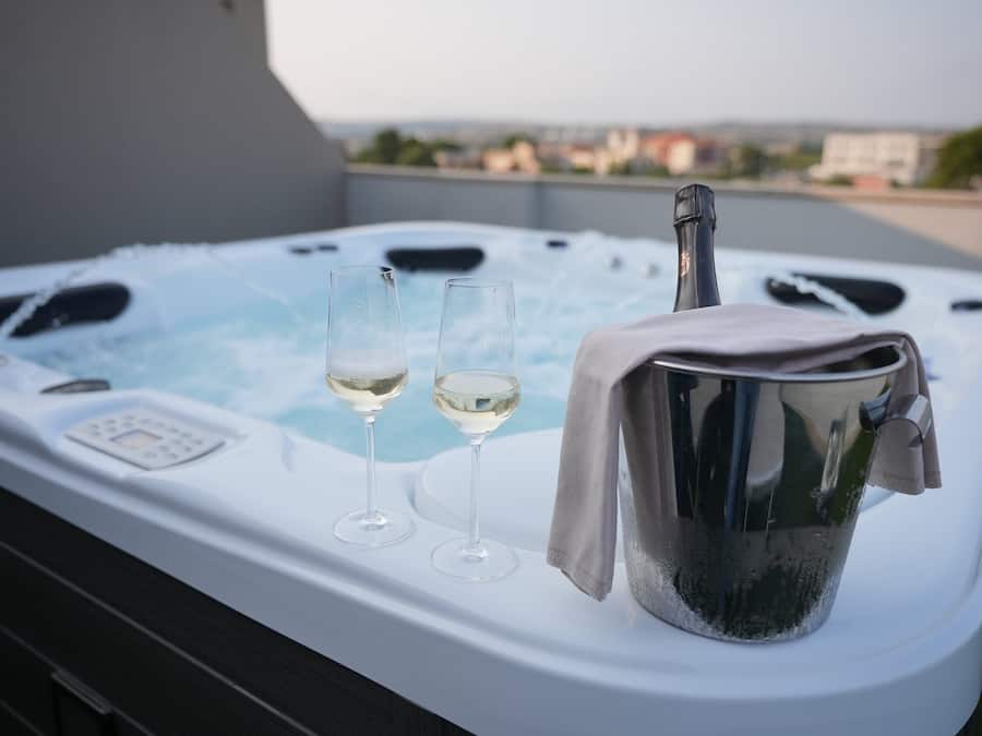 A hot tub with two glasses of white wine and a bucket of ice.