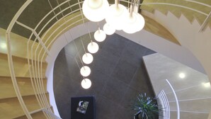 Una escalera en espiral moderna con una plataforma central, rodeada por una barandilla blanca y lámparas colgantes.