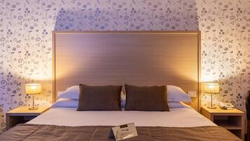 Ein ordentlich bezogenes Bett mit Holz-Kopfteil, zwei Nachttischlampen und einem blumigen Wandpapier.