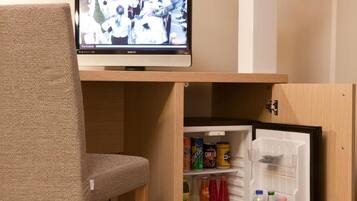 A television mounted on a wooden shelf above a refrigerator stocked with beverages and snacks.